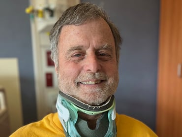 Ira Egan smiles while wearing a cervical collar in his patient room.