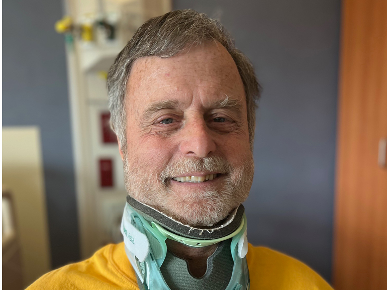 Ira Egan smiles while wearing a cervical collar in his patient room.