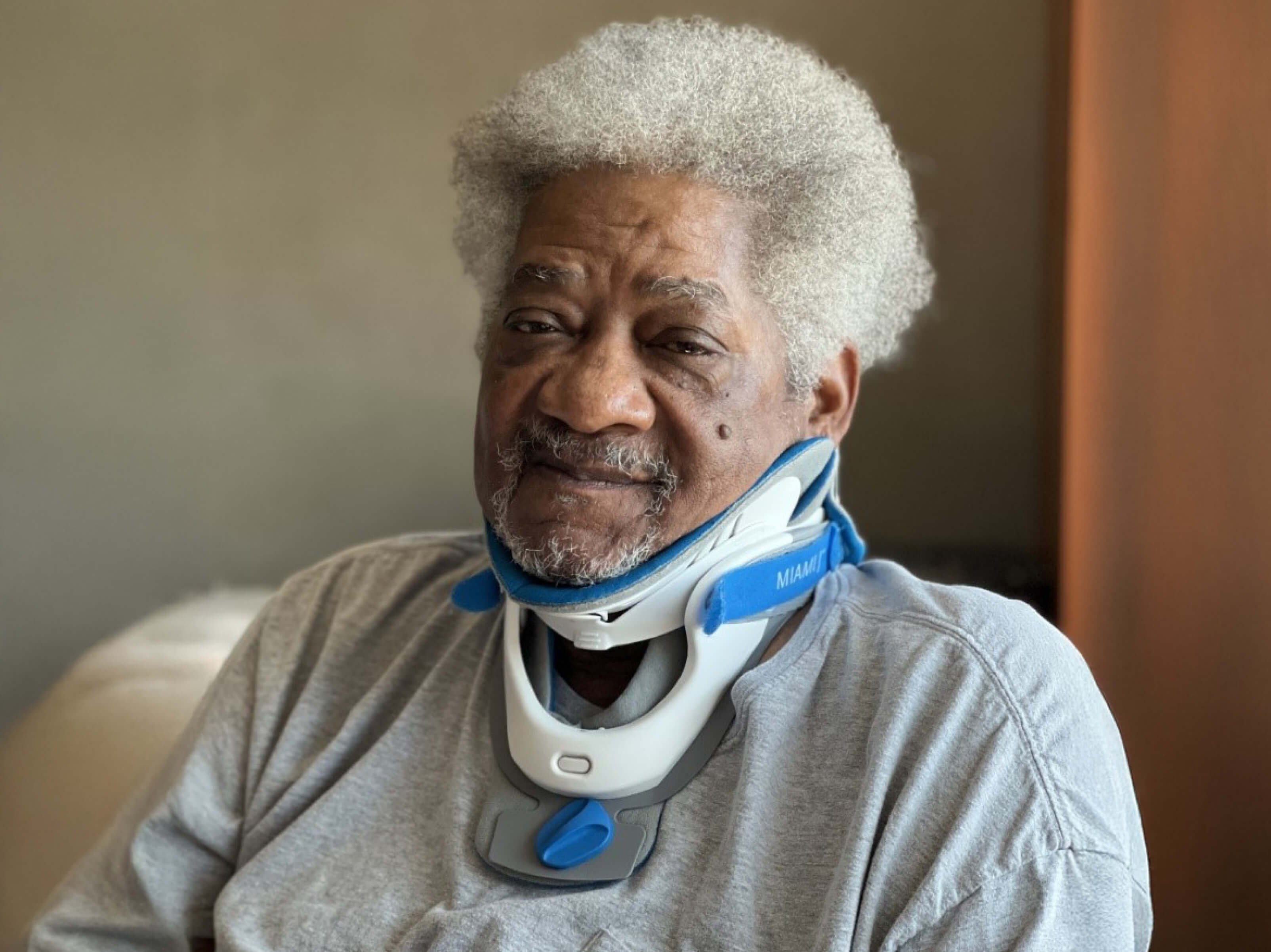 Willie Wilson, wearing a neck brace, sits in a chair and looks at the camera.