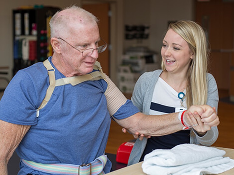Female therapist supporting the arm of a man wearing a rotator cuff brace.