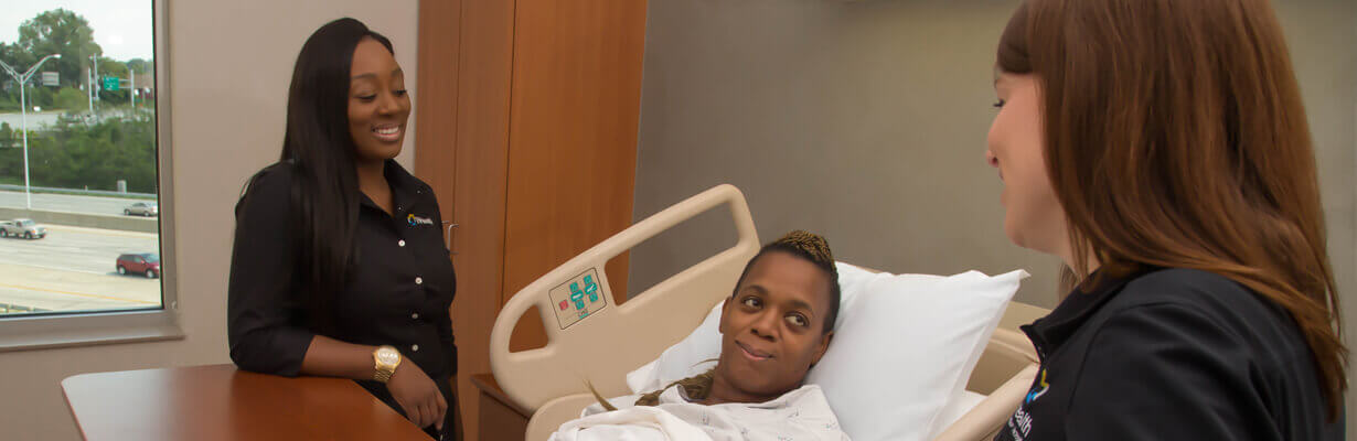 Female therapist talking to a young woman lying in hospital bed.