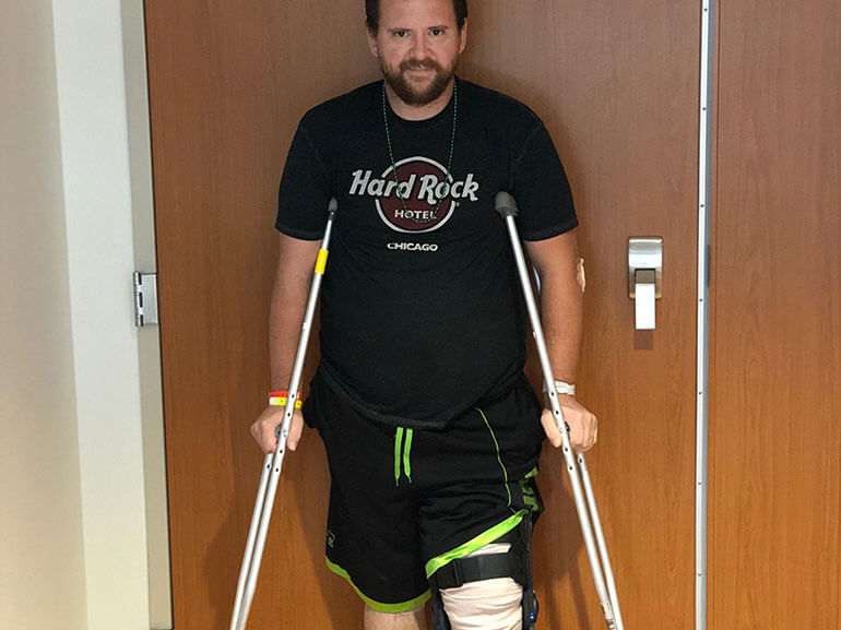 Brandon in a Hard Rock Cafe black t-shirt and standing with crutches.