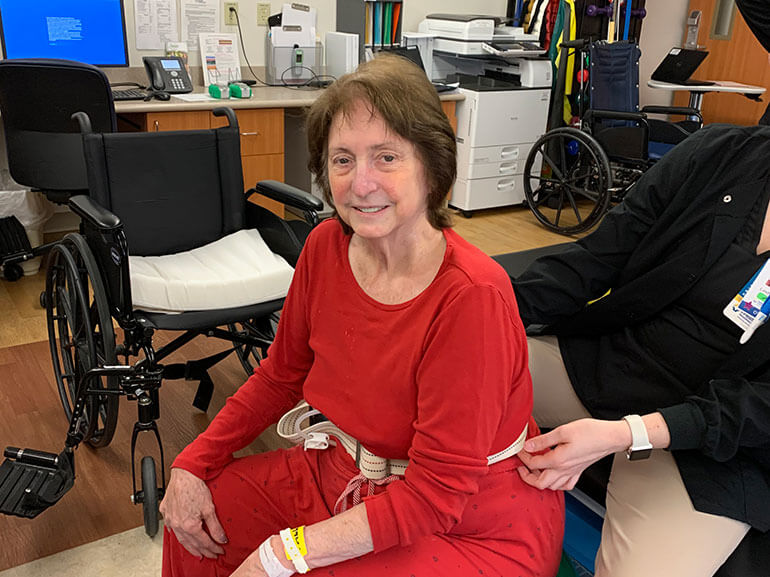 Linda wearing a red sweatsuit and sitting in a therapy gym.