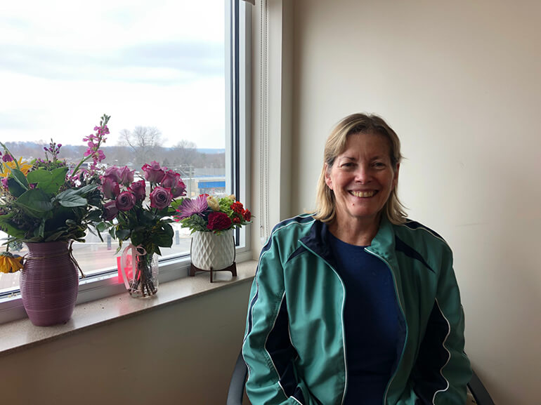 Ruth Ann wearing a green jacket and sitting in a chair by a window in her hospital room.