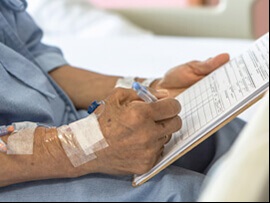 Close up view of elderly hand with an IV line attached signing a paper.