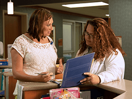 Two nurses talking at a nurse's station in a hospital.