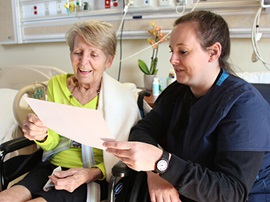 A female therapist reviewing a form with female patient sitting in a wheelchair.