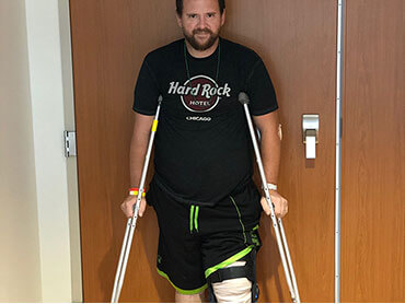 Brandon on crutches standing next to a door in a hospital hallway.