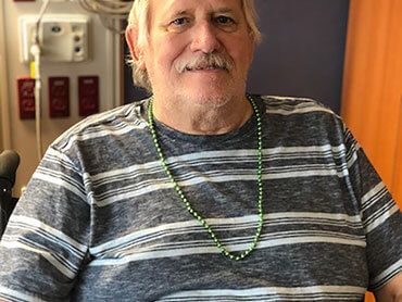 Gerald wearing a necklace of small green beads and sitting in hospital room.