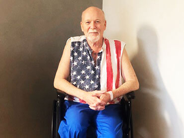 Man wearing a sleeveless American flag t-shirt sitting in a wheehchair.