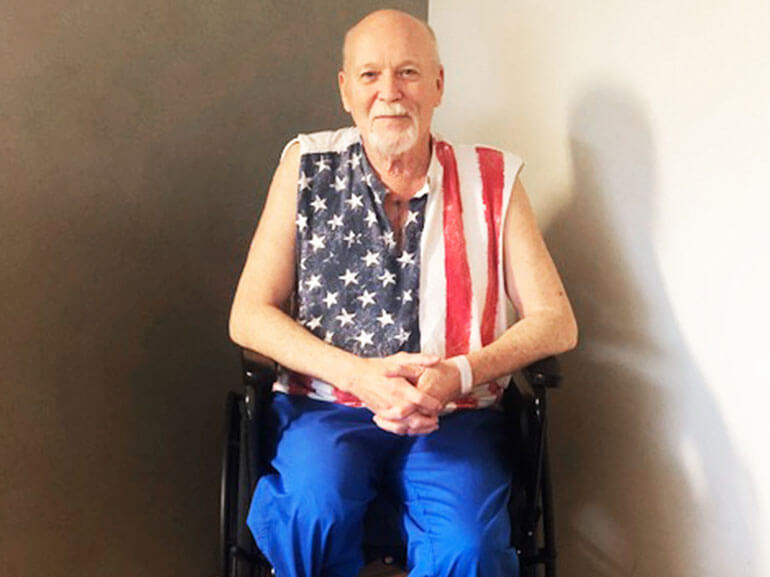 Bernie wearing a sleeveless American flag t-shirt sitting in a wheehchair.