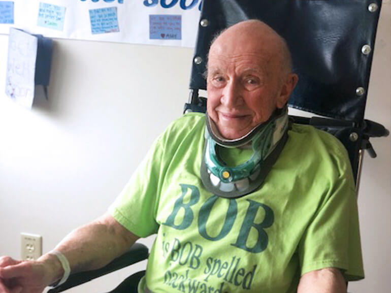 Bob in a green t-shirt wearing a neck brace sitting in a hospital room.