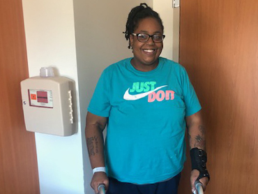 Woman wearing a turquoise Just Do It t-shirt and standing with the help of a walker.