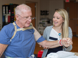 Female therapist supporting the arm of a man wearing blue t-shirt and a soft shoulder brace.