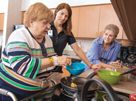 A woman holding a small blue bowl in a therapy kitchen setting.