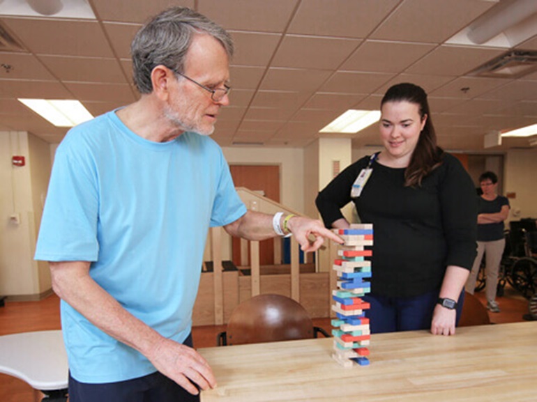 White-haired man wearing glasses working with colored therapy blocks in a wood stacking game.